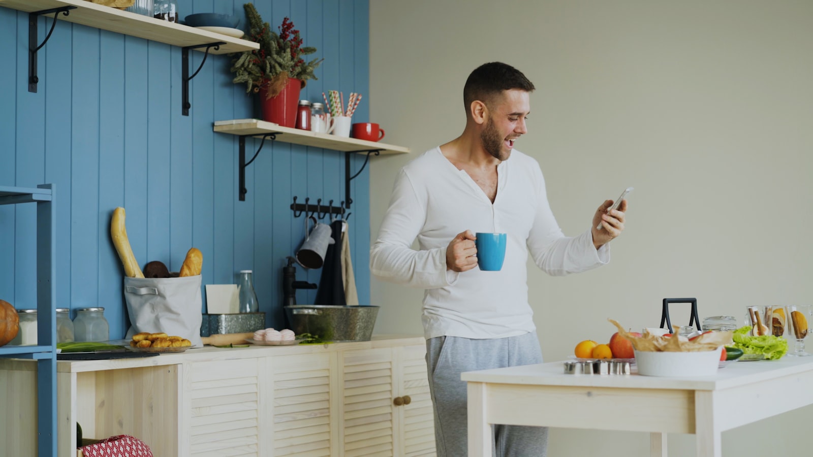 Mand står i sit køkken med en kop kaffe og læser nyheder på telefonen om morgenen