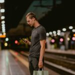 Mand set skråt bagfra tjekker sin mobil på en metroperron i køligt kunstlys