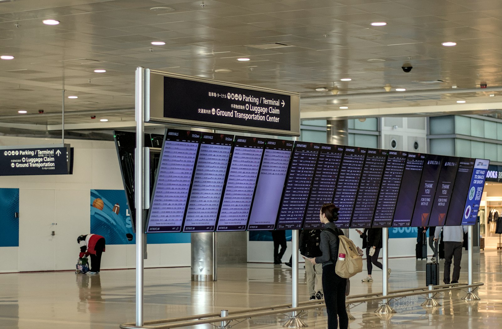 Rejsende med rygsæk set bagfra foran en stor afgangstavle med flyinformationer i en lufthavnsterminal