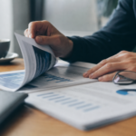 Hænder blader gennem et printet whitepaper på et skrivebord med læsebriller og en kop kaffe i baggrunden