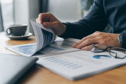 Hænder blader gennem et printet whitepaper på et skrivebord med læsebriller og en kop kaffe i baggrunden