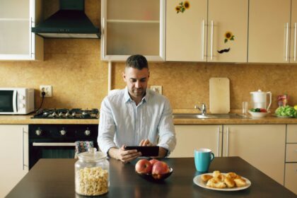 Mand ved køkkenbord om morgenen ser på en tablet mellem morgenmad og kaffe