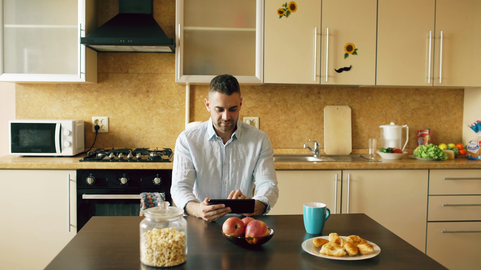 Mand ved køkkenbord om morgenen ser på en tablet mellem morgenmad og kaffe