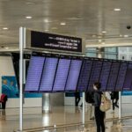 Rejsende med rygsæk set bagfra foran en stor afgangstavle i en lufthavn
